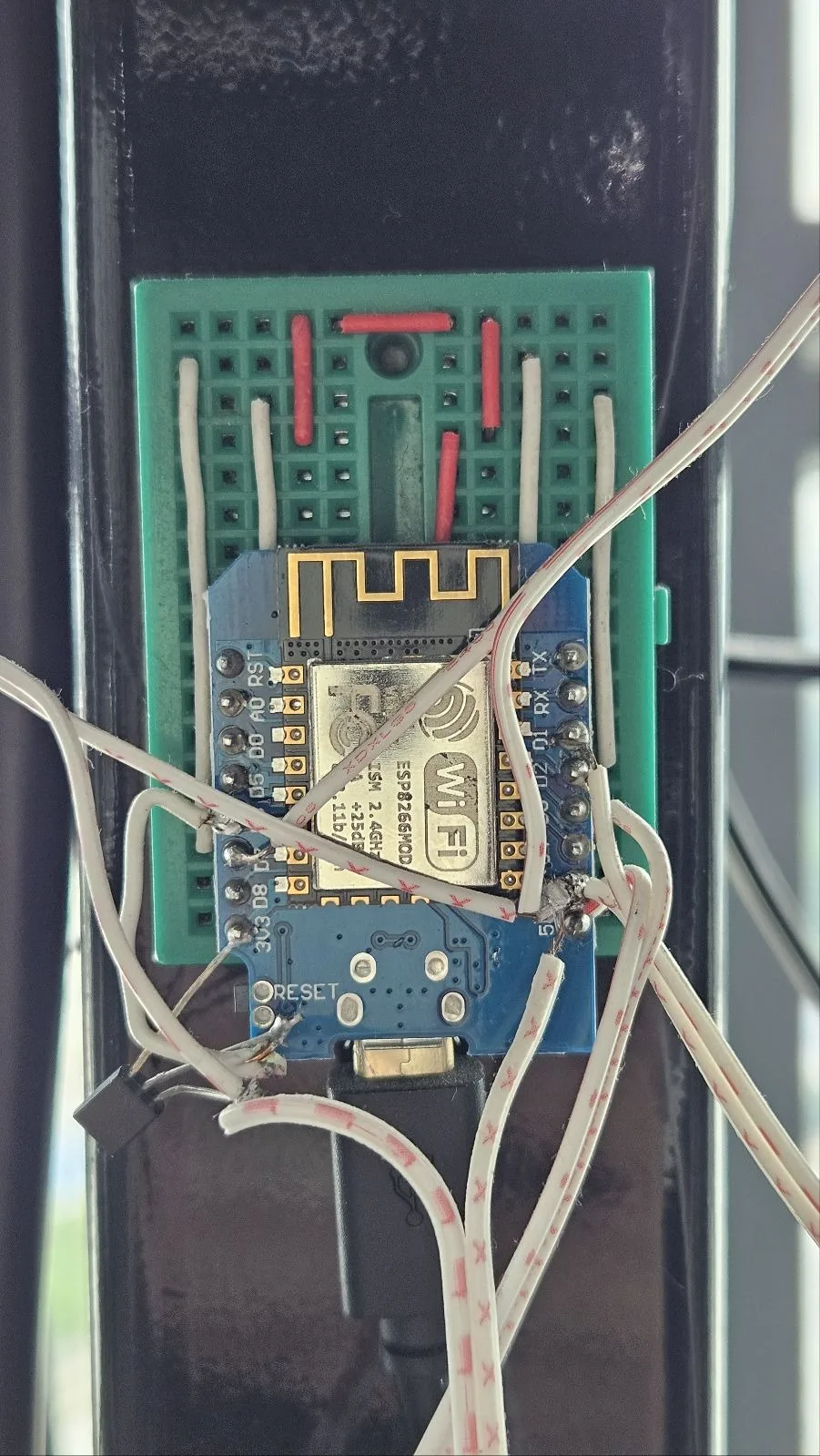 A Wemos D1 Mini ESP8266 on a small green breadboard, cable-tied to a TV bracket pole, with hand-soldered twisted-pair wires running out to infrared LEDs.
